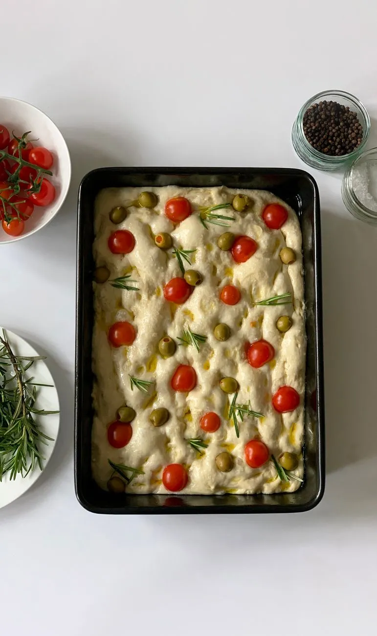 Sirova focaccia u limu s cherry rajčicama, maslinama i ružmarinom, prije pečenja