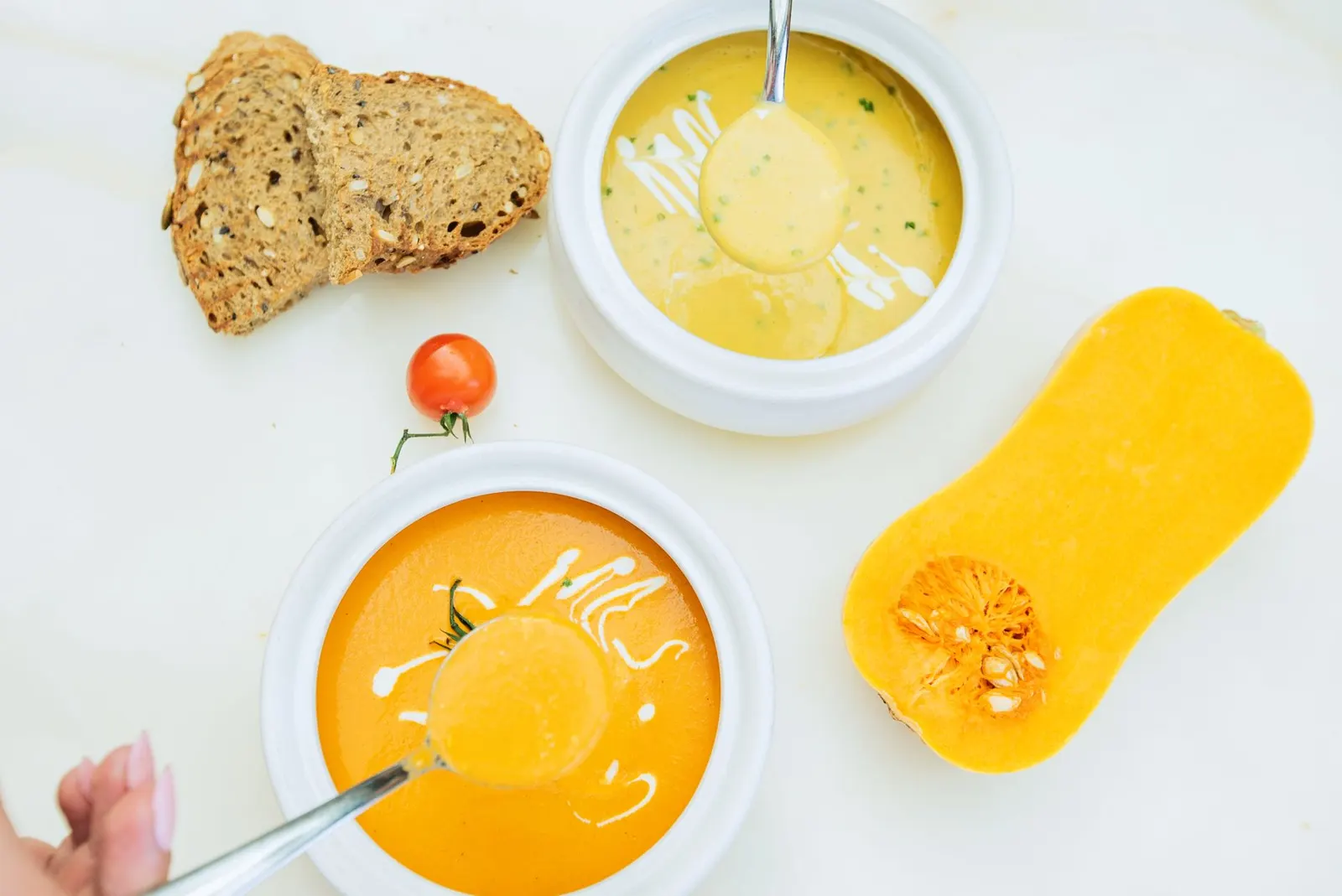 Dvije zdjele krem juhe od bundeve, kriške integralnog kruha i pola butternut tikve na bijelom stolu